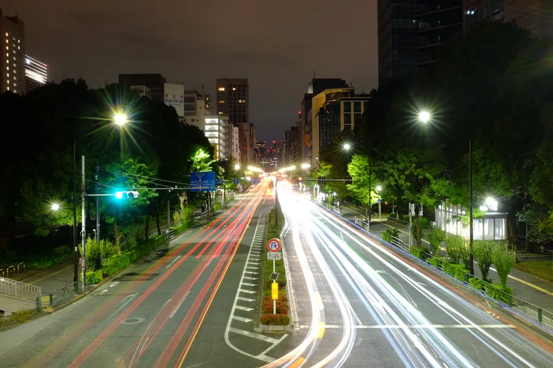 Long exposure photograph of a Tokyo boulevard at night, red and white light trails stretching into the distance