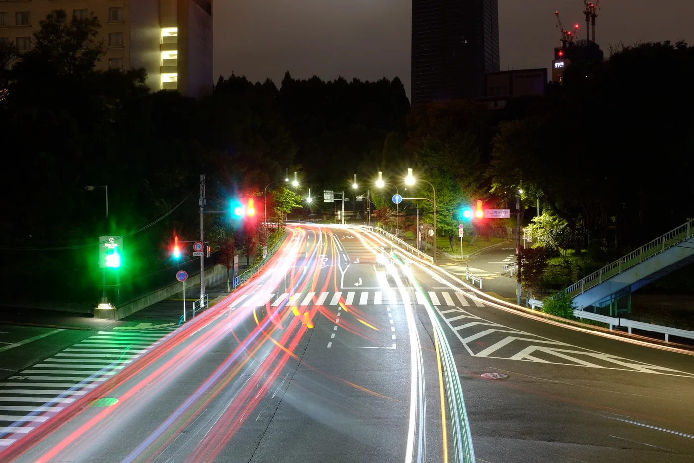 Long exposure photograph of a Tokyo intersection at night, coloured light trails crossing at traffic lights